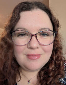 An image of Amy Davidson. She is a woman in her mid 30s with curly red hair and glasses.