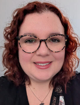 An image of Amy Davidson. She is a woman in her mid 30s with curly red hair and glasses.